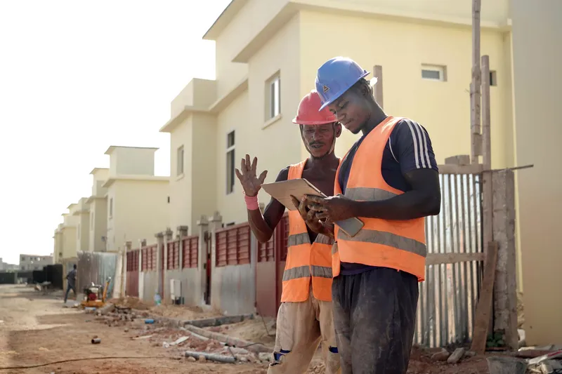 Two site workers in high-visibility vests reviewing project progress on a tablet