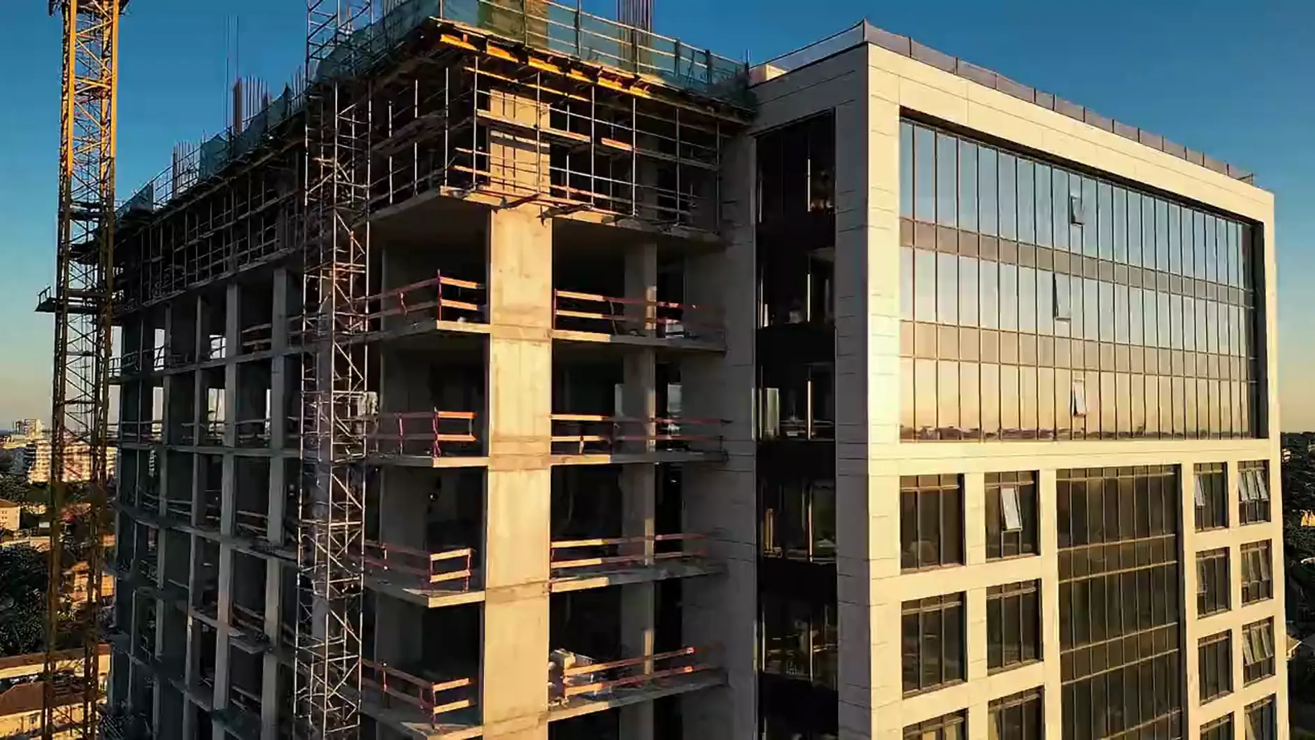 A multi-storey building under construction at golden hour, its exposed concrete frame giving way to a finished glass facade